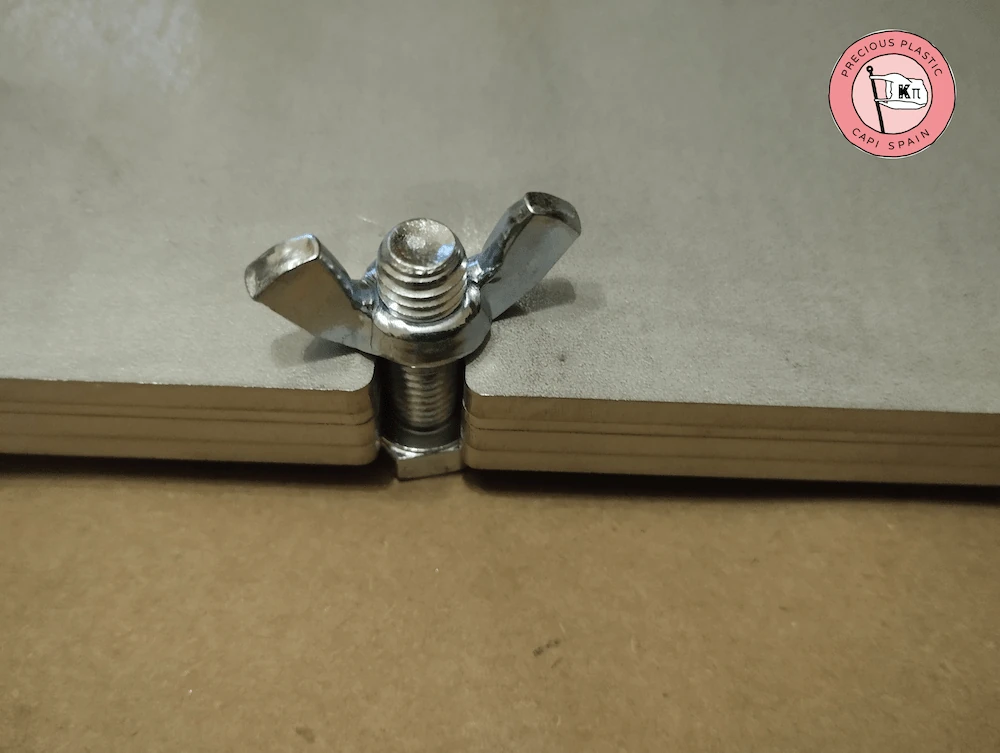 Detalle de cierre rápido con tornillo y tuerca de mariposa de acero inoxidable en el lateral de un molde modular A4.