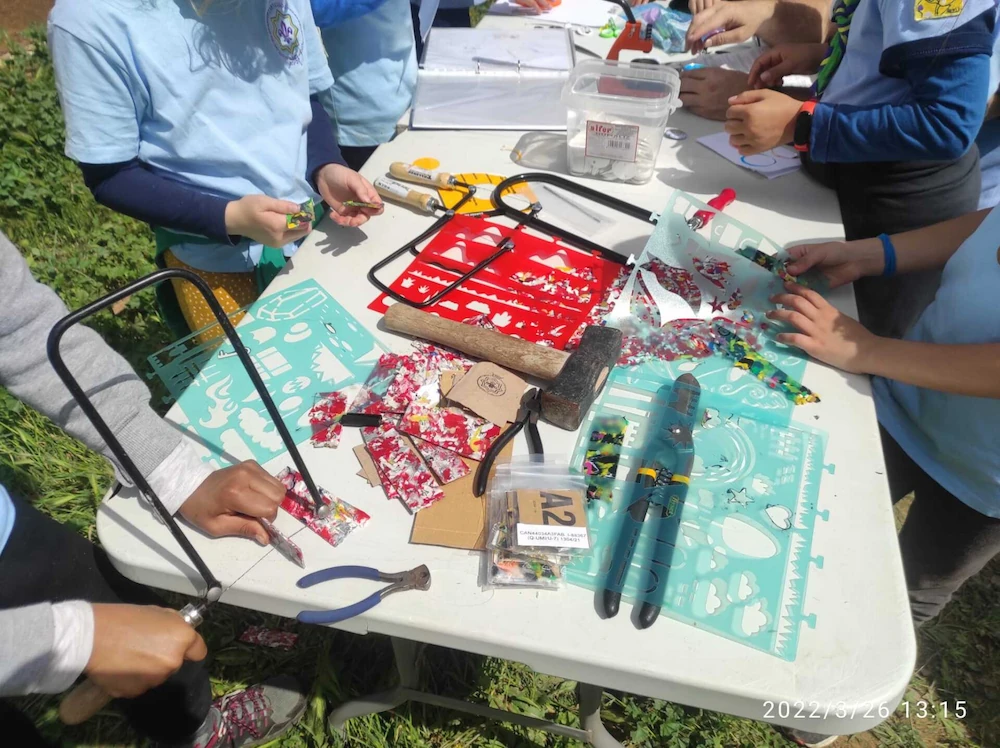 Taller educativo al aire libre donde se cortan y manipulan láminas de plástico reciclado con seguetas y herramientas manuales.