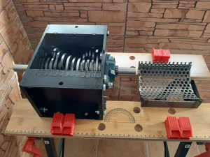 Precious Plastic V2.1 shredder box next to its curved filtering sieve and removable tray on a workbench.